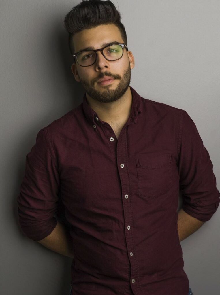 Man in red shirt with glasses holds hands behind his back